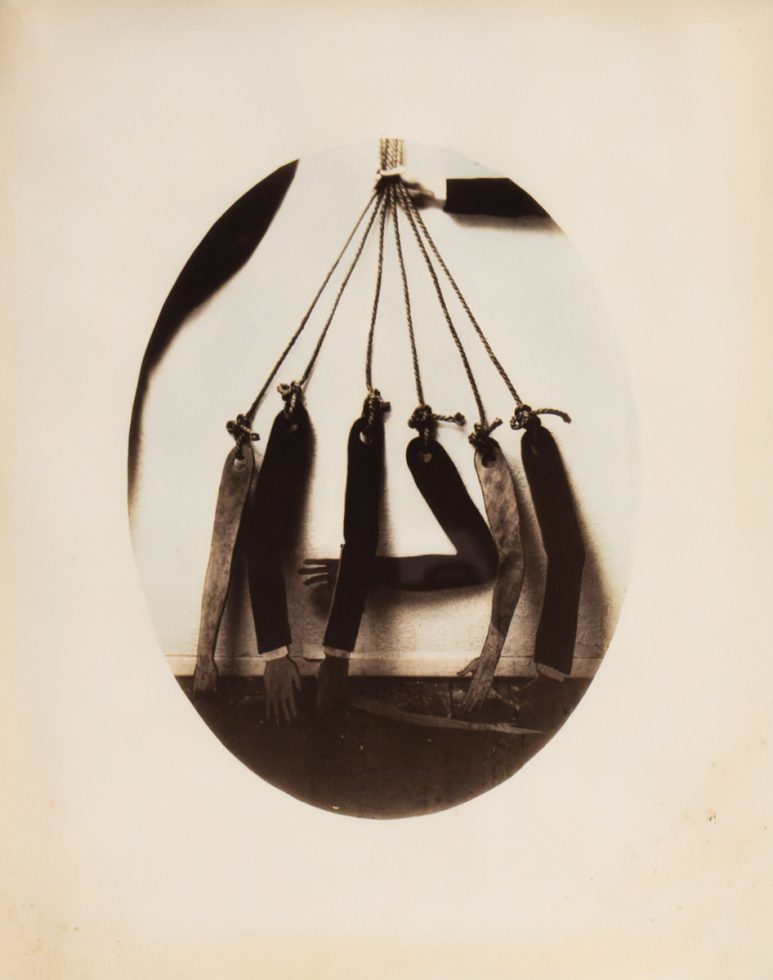 This is an old, somewhat blurry black and white photo of seven dismembered arms hanging by strings.