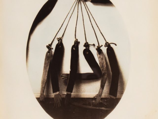 This is an old, somewhat blurry black and white photo of seven dismembered arms hanging by strings.