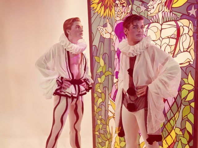 Click for sizes / editions / prices. Two pale-skinned performers in white ruffled collars and harlequin-style costumes stand before a colorful stained-glass panel depicting figures.