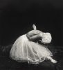 A lone figure, draped in white, kneels with bowed head and upraised hands against a dark void, evoking a sense of sorrow or profound contemplation.