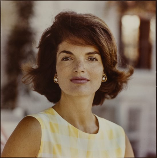 A color photograph of a woman with shoulder length brown hair and a yellow and white gingham dress.