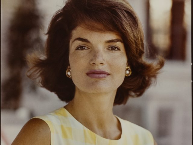 A color photograph of a woman with shoulder length brown hair and a yellow and white gingham dress.