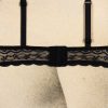 The image shows the back closure and straps of a black lace bra. The fabric features a delicate, floral lace design with scalloped edges and adjustable shoulder straps. The bra is fastened with a standard hook-and-eye closure. It is displayed on a neutral, textured background, likely a mannequin or fabric-covered form.