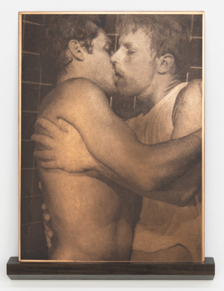 This framed artwork on a dark wooden shelf depicts two individuals embracing in a kiss, rendered in a distinctive halftone pattern.