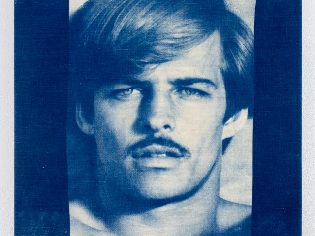 Blue-toned portrait of a shirtless man with parted hair and a mustache, printed on textured canvas with a photographic, vintage appearance.