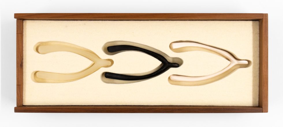 A wooden box with three wishbone shaped objects inside it.