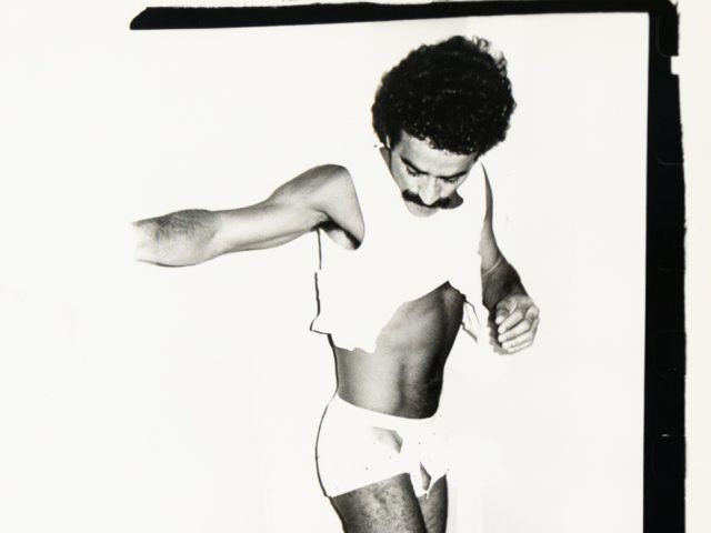 A monochrome image captures a person in a state of undress, with a lifted top and bulky leg wear around their ankles.