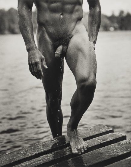 A black and white photograph of a nude man walking out of a lake.