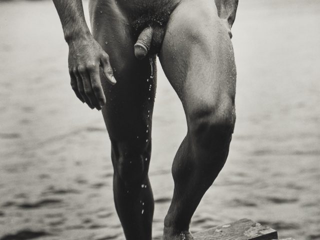A black and white photograph of a nude man walking out of a lake.
