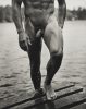 A black and white photograph of a nude man walking out of a lake.