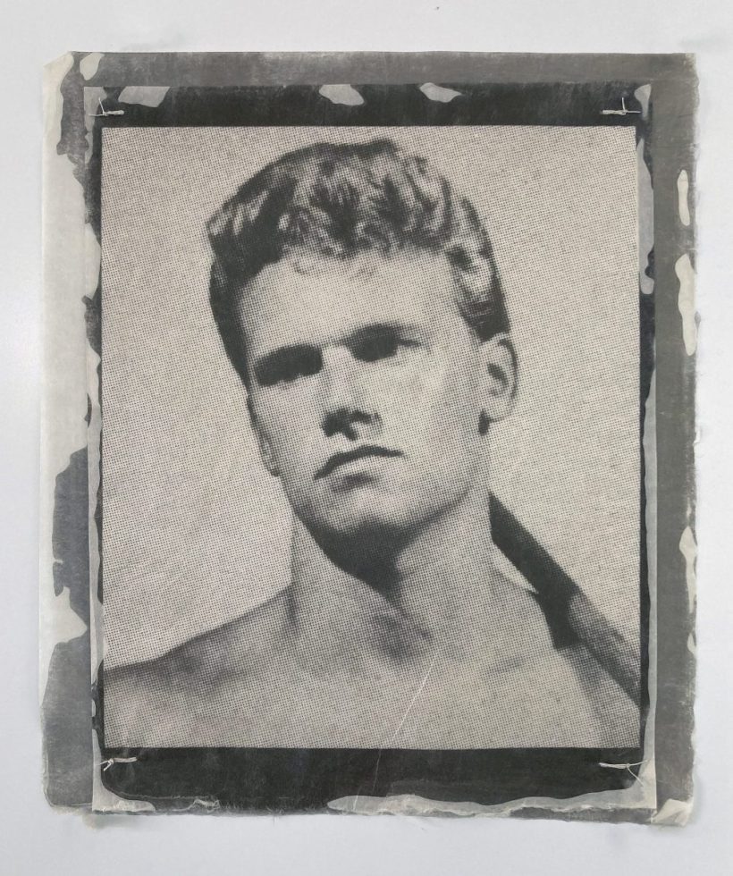 This close-up, black and white portrait features a young man with light hair and serious eyes, his image rendered on what appears to be a textured fabric or paper.