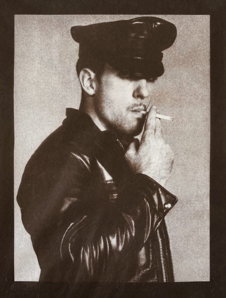 A male figure in a leather outfit smoking a cigarette.