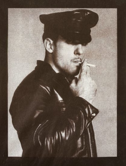 A male figure in a leather outfit smoking a cigarette.