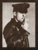 A male figure in a leather outfit smoking a cigarette.