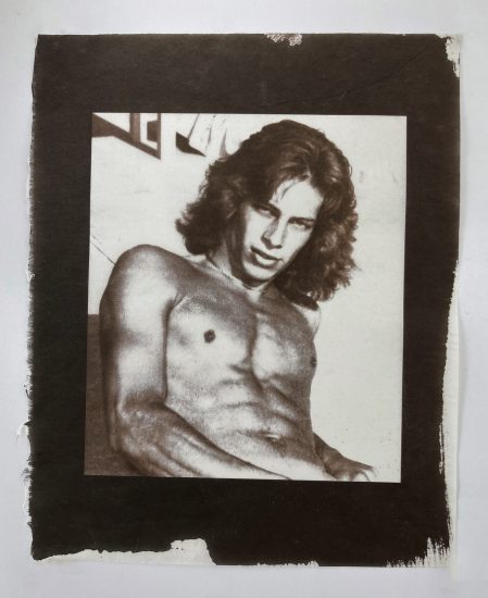 A gold-toned monochromatic portrait shows a shirtless man with wavy hair, looking directly at the viewer with an intense gaze.
