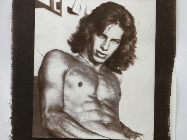 A gold-toned monochromatic portrait shows a shirtless man with wavy hair, looking directly at the viewer with an intense gaze.
