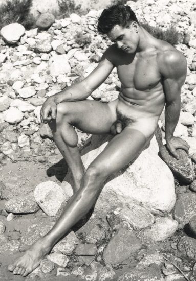 ChatGPT said: A black-and-white photograph of a nude male figure seated on a large rock in a rocky outdoor setting, looking downward with a contemplative expression.