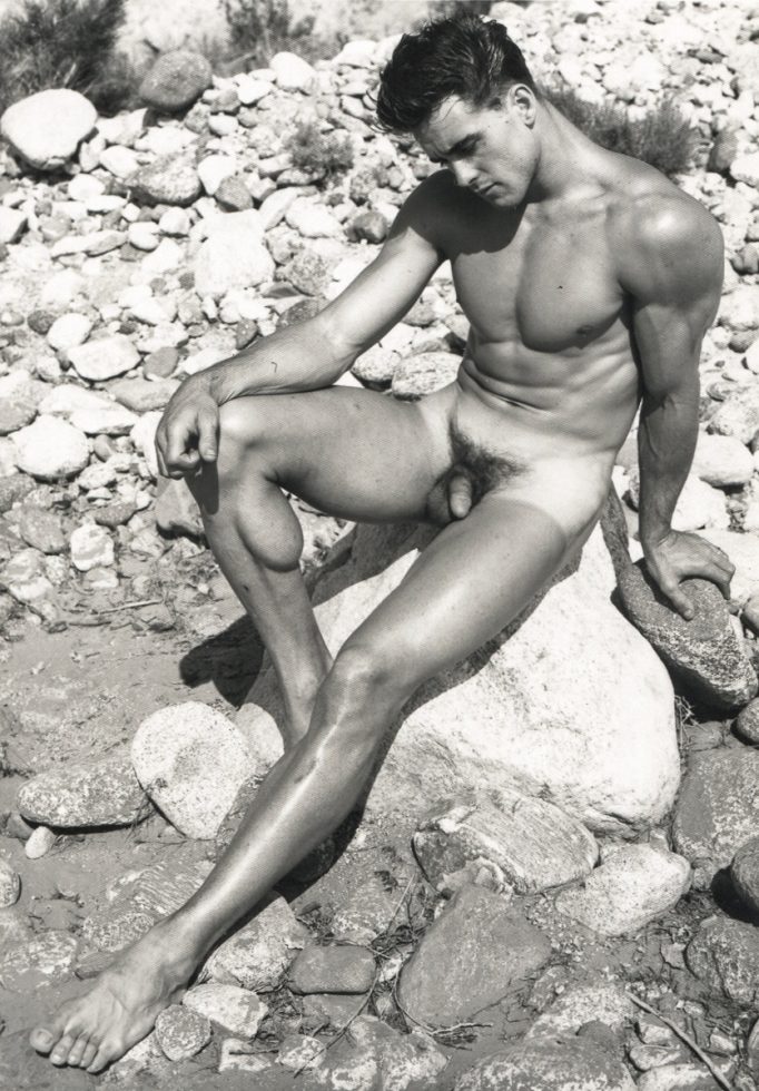 ChatGPT said: A black-and-white photograph of a nude male figure seated on a large rock in a rocky outdoor setting, looking downward with a contemplative expression.