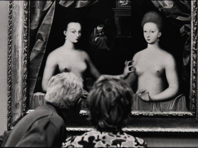 Two people view a painting of two women, creating a playful overlap between the gallery scene and the artwork.