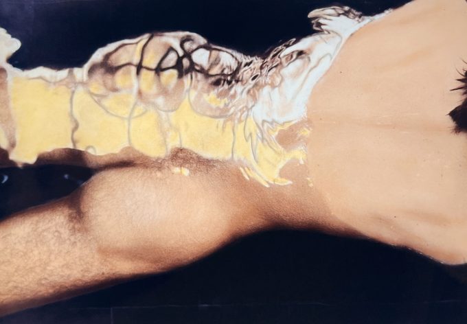A colorful photograph of a nude man's buttocks and torso floating in the water with a reflection.