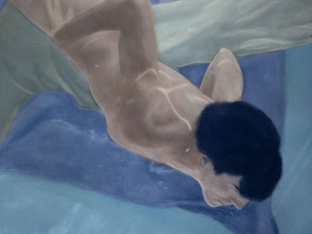 A colorful photograph of a nude man with dark hair swimming underwater.