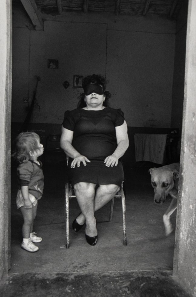 A black and white photograph of a woman sitting in a chair with a child sitting next to her.