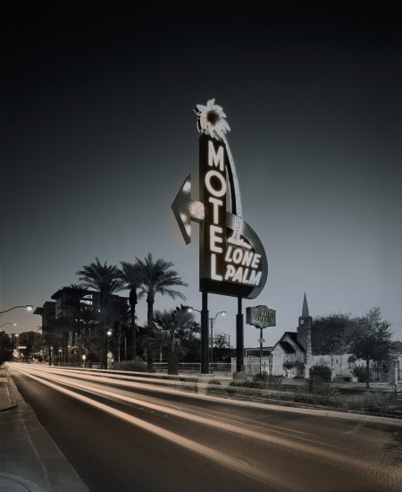 A huge motel sign with glowing neon letters on the side of a main road with blurry car lights.
