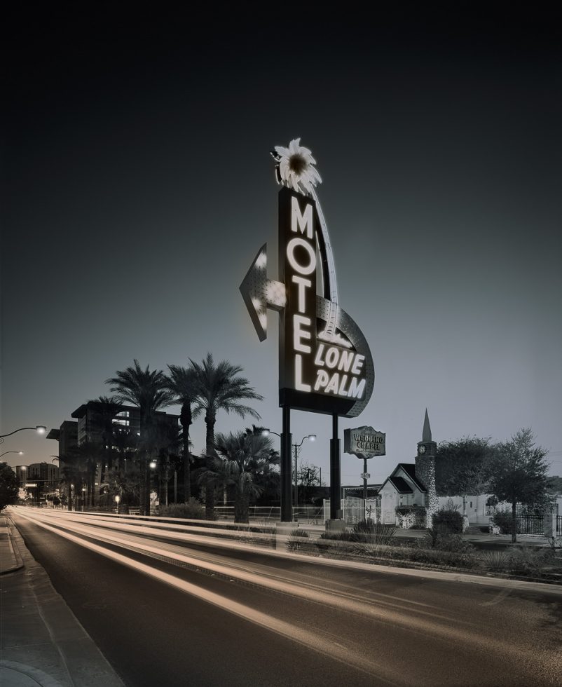 A huge motel sign with glowing neon letters on the side of a main road with blurry car lights.