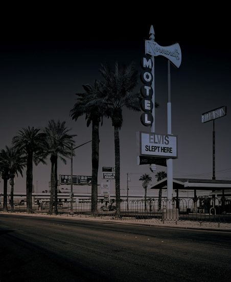 A photograph of a motel sign with palm trees lining the street in front.