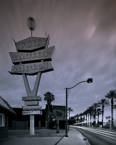 A moody photograph of a motel sign with an empty street and clouds above.