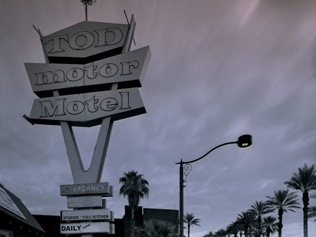 A moody photograph of a motel sign with an empty street and clouds above.
