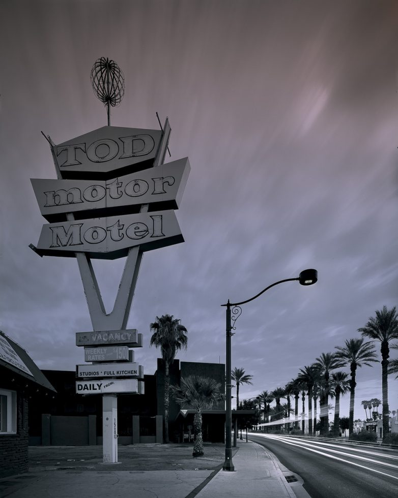 A moody photograph of a motel sign with an empty street and clouds above.