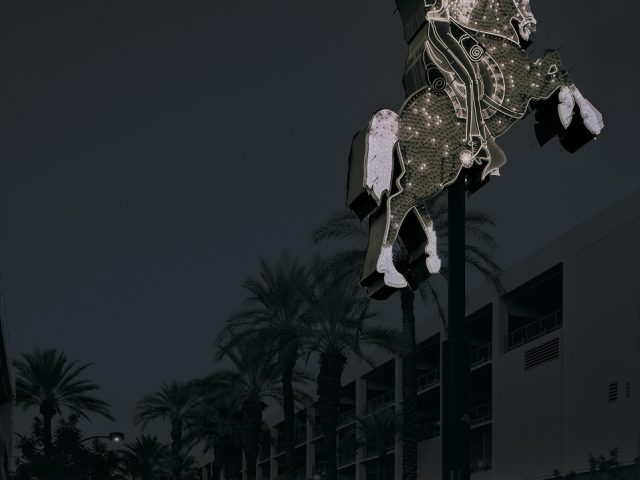 A photograph of a glittering sign for a motel with a man riding a horse.