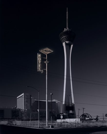 A photograph of a super tall motel sign in front of a spire.