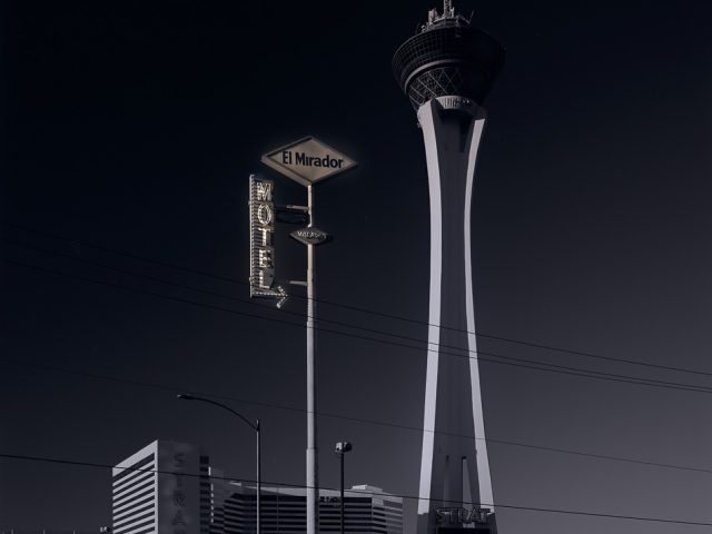 A photograph of a super tall motel sign in front of a spire.