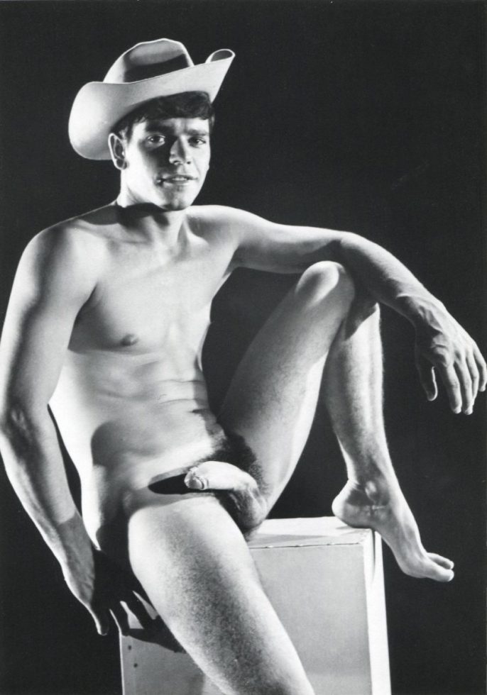 A black and white portrait of a nude young man sitting on a pedestal wearing a cowboy hat.