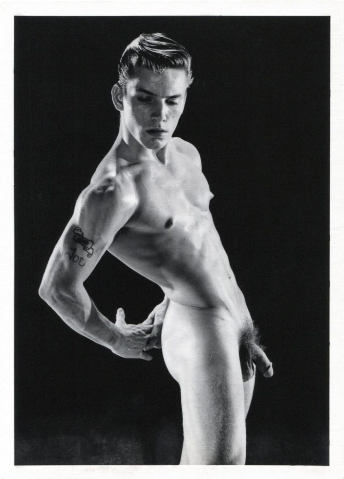A black and white photograph of a handsome nude young man in a studio setting.
