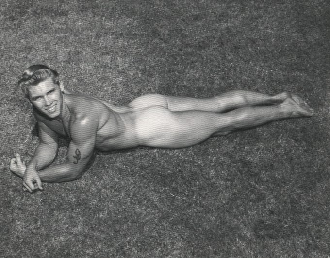 A black and white photograph of a handsome nude young man lying in the grass.