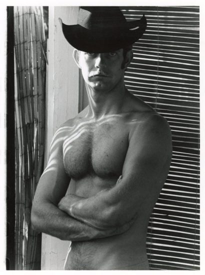 A black and white photograph of a shirtless man in a black cowboy hat.