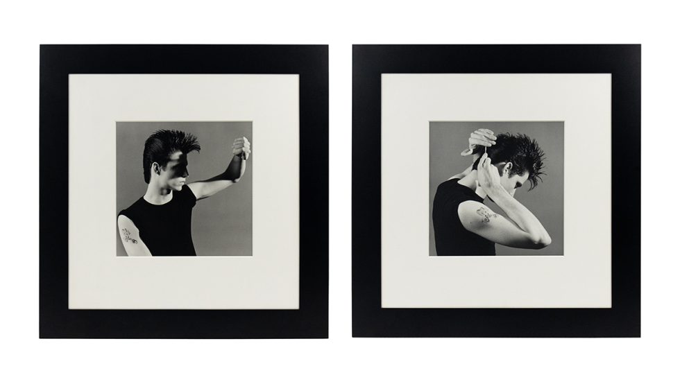 Two black-and-white photographs of the same man in a sleeveless black shirt displayed in white mats and wide black frames.