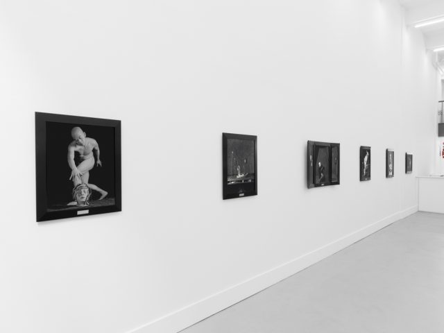 A photograph of black and white photographs in black frames hanging in a contemporary gallery setting.