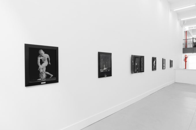 A photograph of black and white photographs in black frames hanging in a contemporary gallery setting.