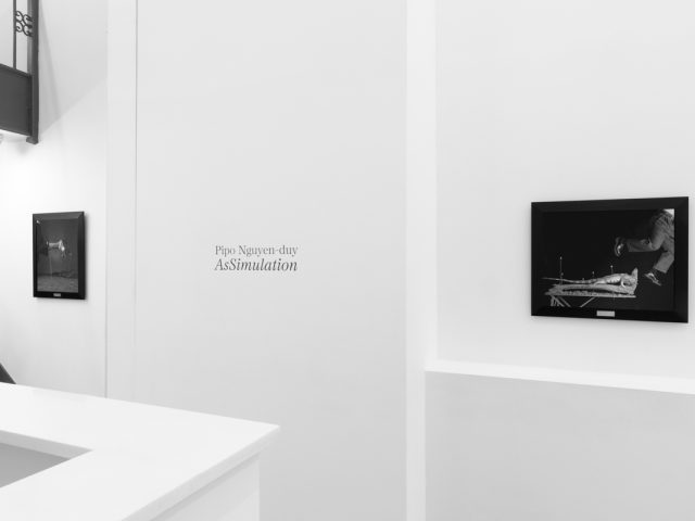 A photograph of black and white photographs in black frames hanging in a contemporary gallery setting.