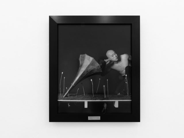 A photograph of black and white photographs in black frames hanging in a contemporary gallery setting.