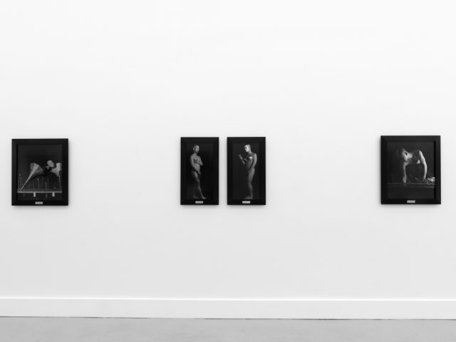 A photograph of black and white photographs in black frames hanging in a contemporary gallery setting.