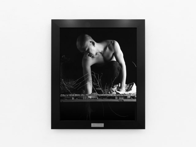 A photograph of black and white photographs in black frames hanging in a contemporary gallery setting.