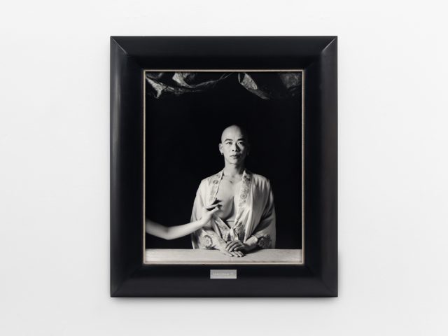 A photograph of black and white photographs in black frames hanging in a contemporary gallery setting.
