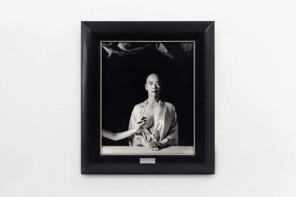 A photograph of black and white photographs in black frames hanging in a contemporary gallery setting.