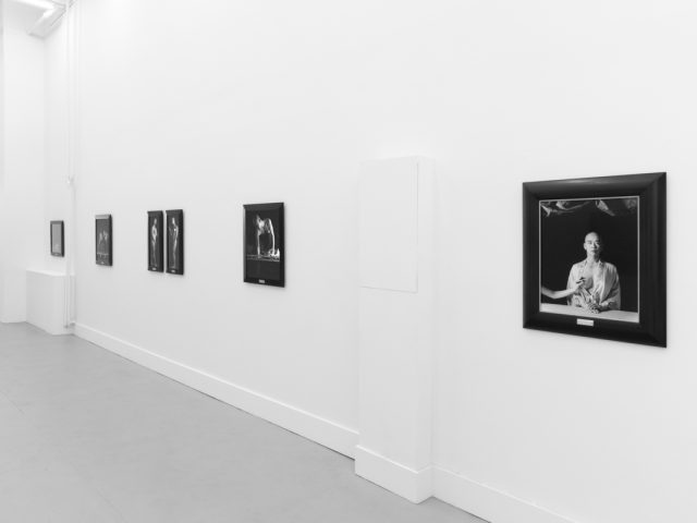 A photograph of black and white photographs in black frames hanging in a contemporary gallery setting.