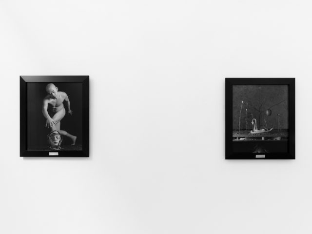 A photograph of black and white photographs in black frames hanging in a contemporary gallery setting.